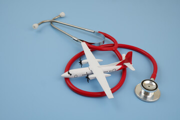 Travel health insurance concept. Airplane model with red stethoscope on blue background.	