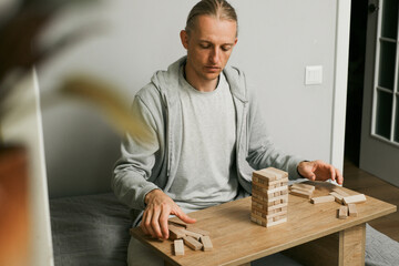 Person is carefully stacking blocks in wooden tower game in the room at home. Digital detox and concentration. Quality time offline