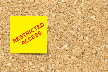 Yellow note paper with word restriced access on cork board background with copy space