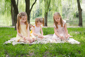 Three children gathered around wooden tower game, focused on stacking blocks, enjoying sunny day in the park. Friends playing tower game outdoors