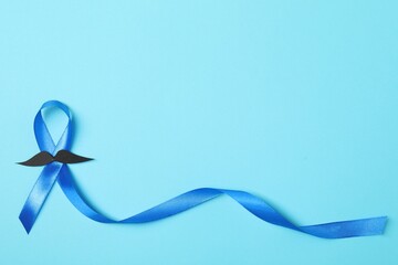 Blue ribbon and fake mustache on color background, top view with space for text. Prostate cancer...