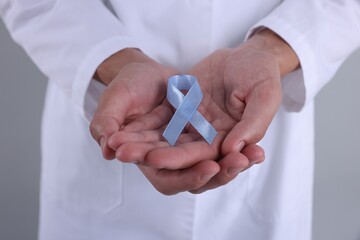 Prostate cancer awareness. Doctor holding light blue ribbon as symbol of support on grey...