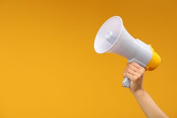 Woman holding megaphone speaker on orange background, closeup. Space for text