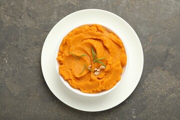 Delicious mashed sweet potatoes with rosemary and nuts in bowl on gray textured table, top view