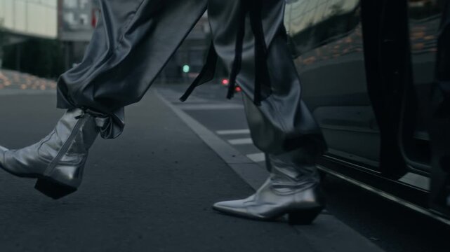 Low section of unrecognizable high-level female celebrity wearing fancy silver cowboy boots and cargo pants getting out of luxury black car when arriving at film premier