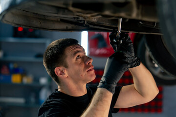 close up an auto mechanic at service station checks a car being lifted on a lift, fixing problems with a mechanical tool the engine part of the lower body
