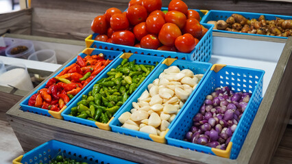 Red peppers, green peppers, garlic, onions, ginger, wooden shelf, blue bins.