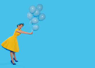 Woman in Yellow Dress Holding Blue Balloons Against Bright Backdrop in Playful Pose