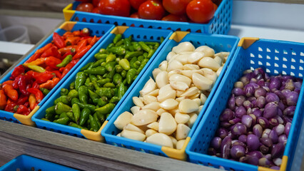 Red peppers, green peppers, garlic, onions, ginger, wooden shelf, blue bins.