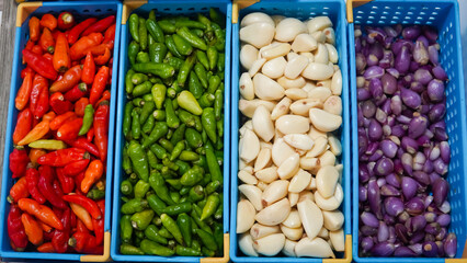 Red peppers, green peppers, garlic, onions, ginger, wooden shelf, blue bins.