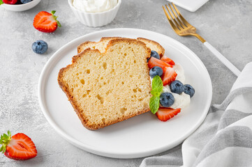 Delicious vanilla pound cake served with fresh berries and whipped cream on a gray concrete background. Selective focus, copy space.