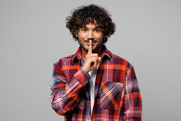 Young happy secret Indian man wear red shirt casual clothes say hush be quiet with finger on lips...