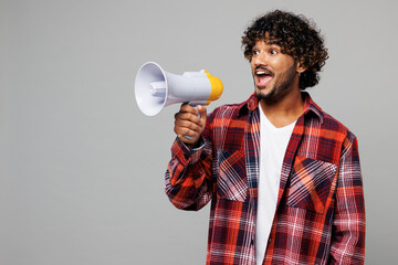 Young happy fun smiling Indian man he wears red shirt casual clothes hold megaphone scream...