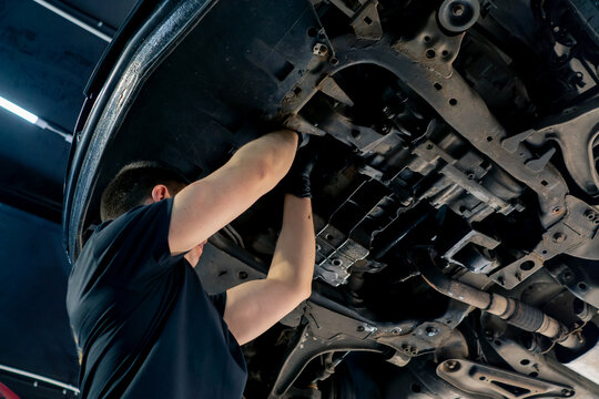 close up an auto mechanic at service station checks a car being lifted on a lift, fixing problems with a mechanical tool the engine part of the lower body