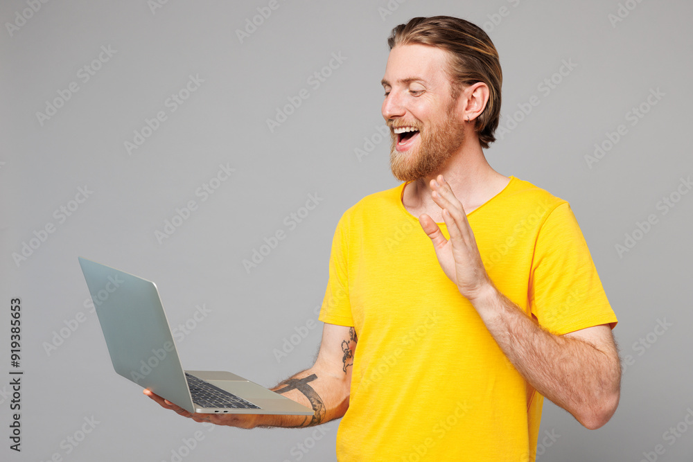 Wall mural Young happy IT man he wear yellow t-shirt casual clothes hold use work on laptop pc computer waving hand get video call talk speak isolated on plain grey background studio portrait. Lifestyle concept.