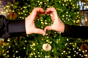 Heart symbol: Hands together of a loving couple on the background of a green Christmas tree with...