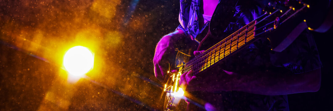 Banner. Musician's hand strums guitar, highlighted by electric blue and purple lights, creating vivid scene of musical passion. Concept of music and party, hobby and work, energy, music festivals. Ad - Powered by Adobe