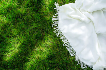 White picnic blanket on a green grass from top view.