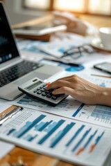 Business professional in gray suit analyzing budget data at desk, surrounded by documents, laptop, and smartphone.