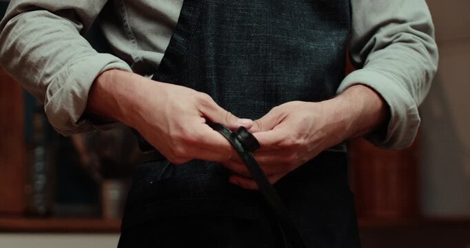 A close-up of men's hands tying the leather belt.