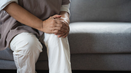 Close up hand of overweight woman arthritis sitting joint ache, sore cramp or sprain tendon in leg on sofa at home, Osteoarthritis chronic disease of body problem from trauma, Health care of knee pain