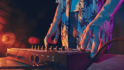 Hands on mixer, bathed in warm neon light, setting stage for night of beats and rhythm, where music...