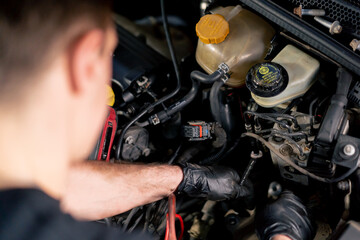 Obraz premium close up in a car service center master in a black T-shirt using tools unscrews the bolts in the engine part of the car replacing spare parts