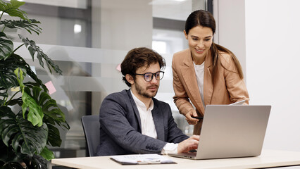 Business team in a modern office using a laptop for financial analysis. They brainstorm and discuss a corporate project, collaborating on solutions. Perfect for teamwork and financial strategy themes.