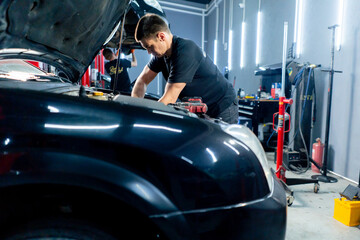 in a car service center master in a black T-shirt using tools unscrews the bolts in the engine part...