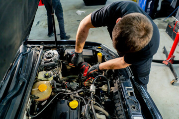 in a car service center master in a black T-shirt using tools unscrews the bolts in the engine part...