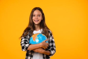 Happy Earth day! Caucasian young teenager schoolgirl pupil student holding hugging globe on geography lesson isolated in yellow background.