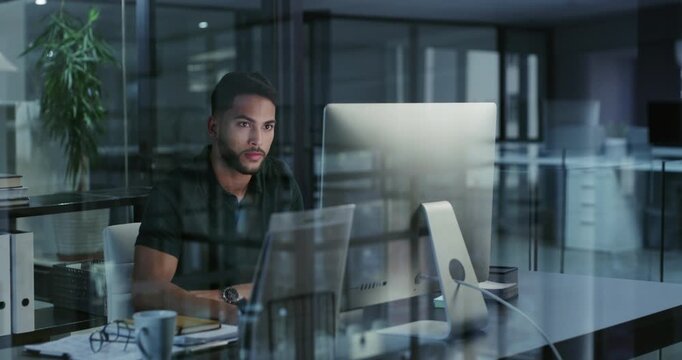 Businessman working late on a computer in an office at night. Young entrepreneur reading emails, research online and compiling reports while planning ideas for deadlines looking satisfied