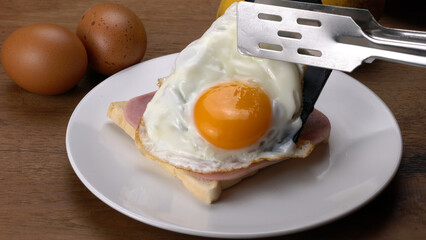 Put a sliced ham and fried egg on a toast in white ceramic dish for breakfast.
