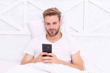 Millennial man use smartphone in bed at home. Man chat on smartphone. Message chatting online. Morning chat. Man read message in bedroom. Browsing social media. Online shopping. Dependence on gadgets