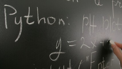 Close up of woman hand writing programming text and formulas on chalkboard, professor writes on blackboard or student solving task. Education and science concept.