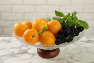 Glass vase with fresh plums, blackberries and mint on white marble table, closeup