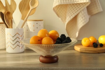 Glass vase with fresh plums and blackberries on wooden table indoors