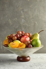 Glass vase with different fresh fruits on gray textured table, space for text