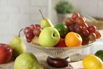 Glass vase with different fresh fruits on table, closeup