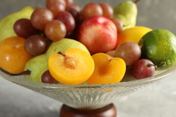 Glass vase with different fresh fruits on gray table, closeup