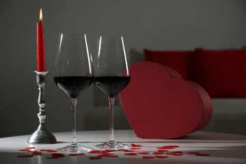 Burning candle, wine in glasses and paper hearts on table indoors