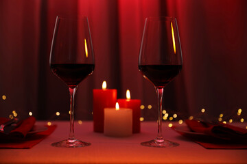 Burning candles and wine in glasses on table against blurred lights