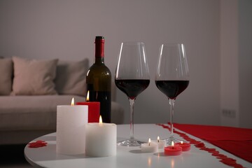 Burning candles, wine and paper hearts on table indoors