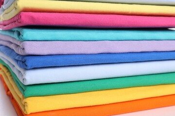 Stack of clean colorful t-shirts on white background, closeup