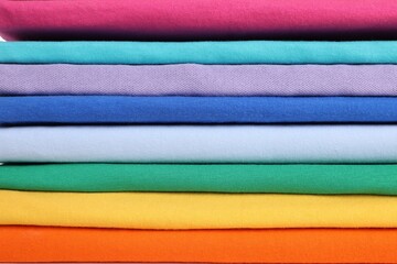 Stack of clean colorful t-shirts as background, closeup