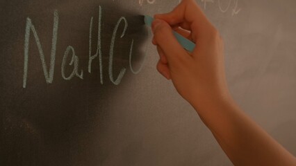 Close up of woman hand writing chemistry formulas on chalkboard, professor writes on blackboard or...
