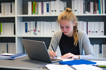 Focused young woman writing notes at her laptop.
