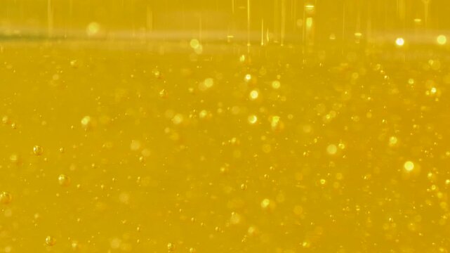 Small air bubbles are trapped in a yellow liquid, creating a sparkling effect. The varying bubble sizes give the liquid a fizzy look, resembling a carbonated drink's effervescence