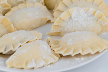 Homemade dumplings on a white plate in flour, close-up.