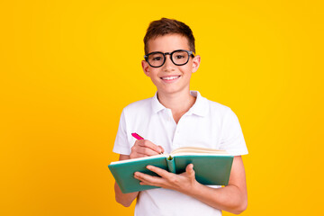 Photo of cheerful positive boy dressed polo t-shirt writing diary emtpy space isolated yellow color background © deagreez
